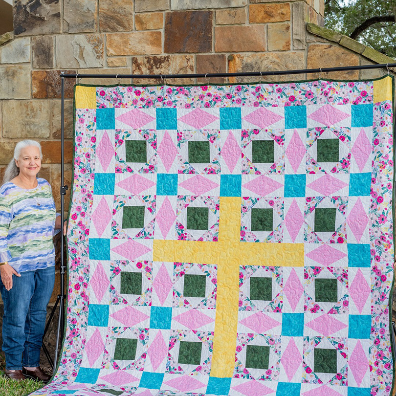 Woman standing next to a hand made quilt.